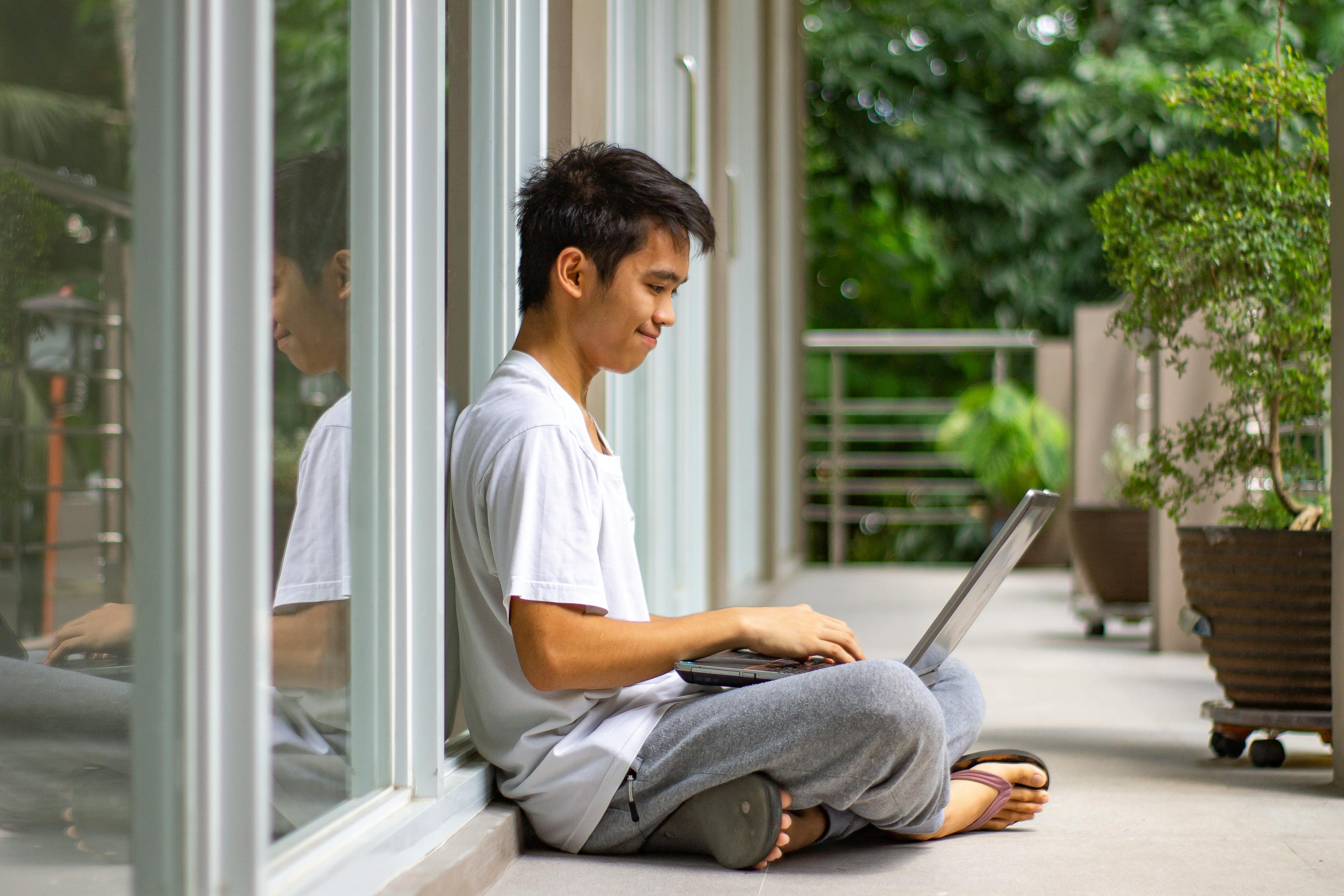 Young man using laptop outdoors for remote work, showcasing modern telecommuting lifestyle.
