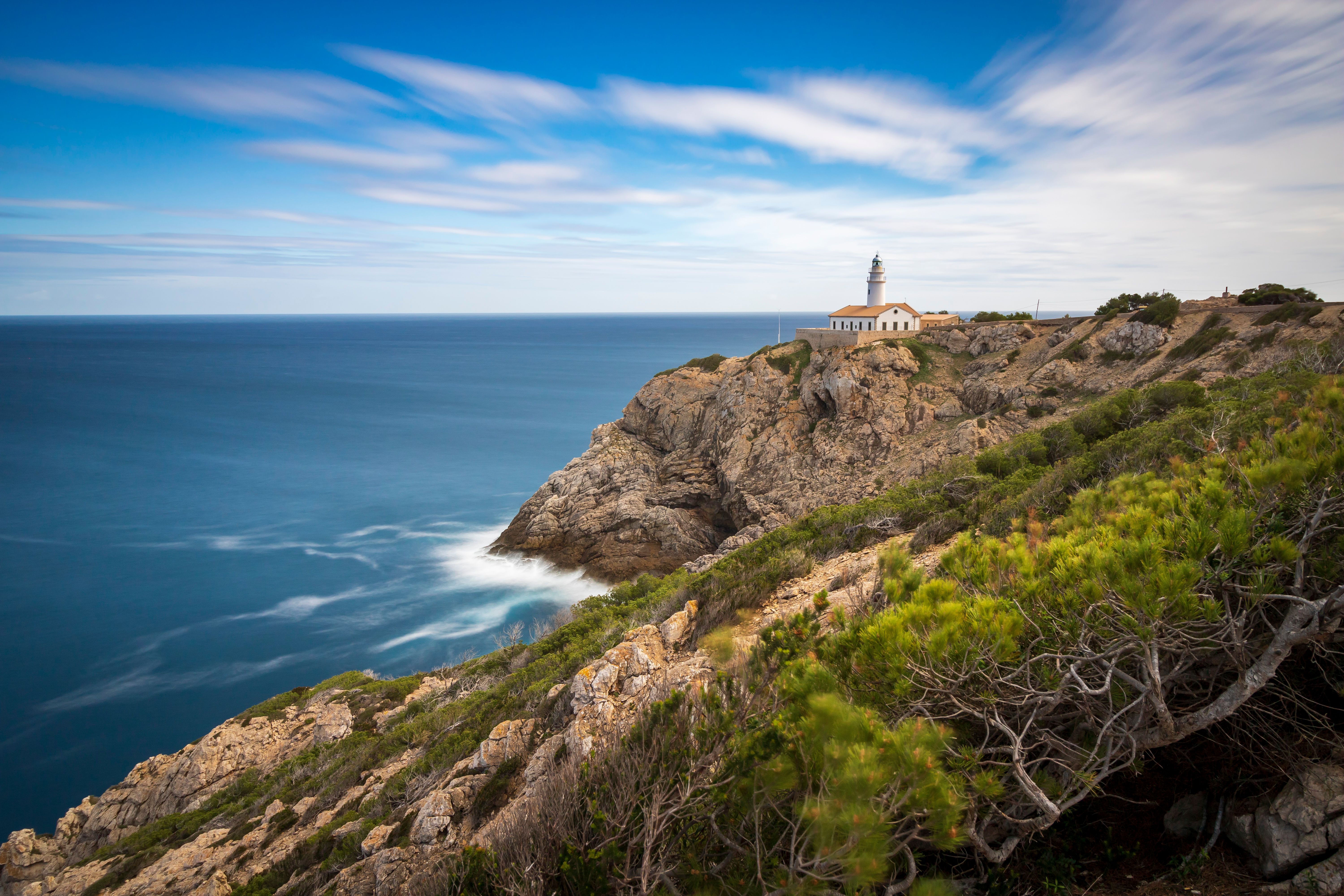 A stunning lighthouse perched on rocky cliffs overlooking the Mediterranean Sea under a clear blue sky.