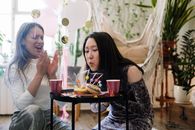 在充满活力的室内生日派对上，一位亚洲女性与朋友一起吹蜡烛，现场配有糖果和装饰品
