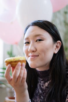 Asian woman holding a doughnut in a festive setting with balloons.
