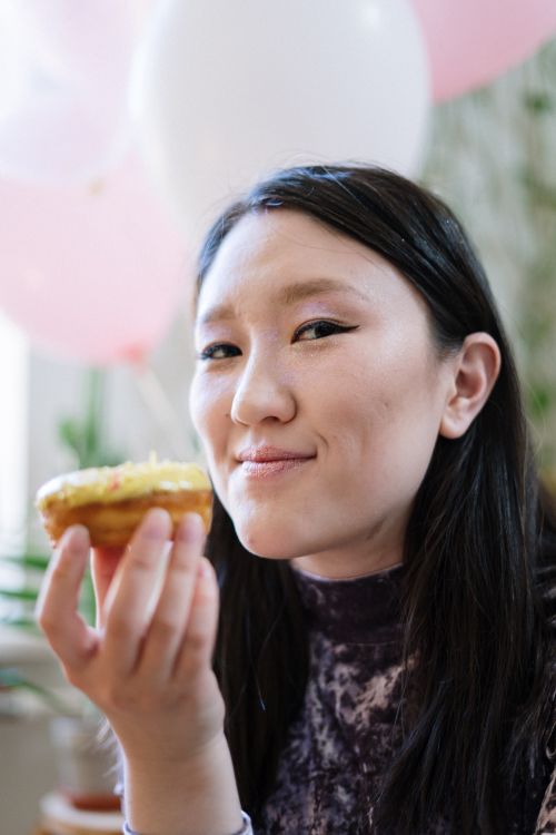 Free Asian woman holding a doughnut in a festive setting with balloons. Stock Photo