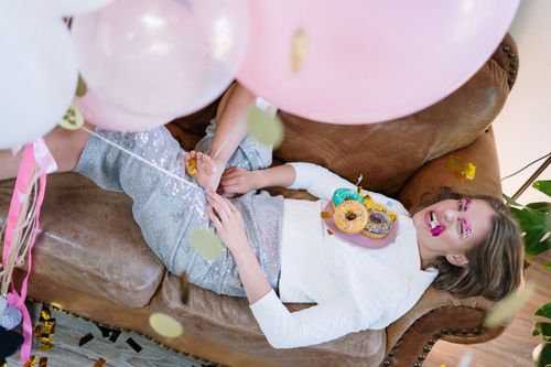Free Young woman relaxing with donuts and balloons on a cozy leather sofa during a festive indoor party. Stock Photo