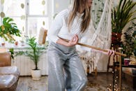 在热闹的室内环境中，一位精力充沛的女人穿着闪闪发光的裤子，用扫帚模仿吉他演奏