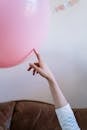 一只手顽皮地触摸着室内的粉红色气球，营造出有趣而节日的气氛