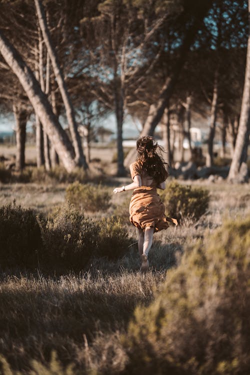 A Woman in Brown Dress Running on Grass Field