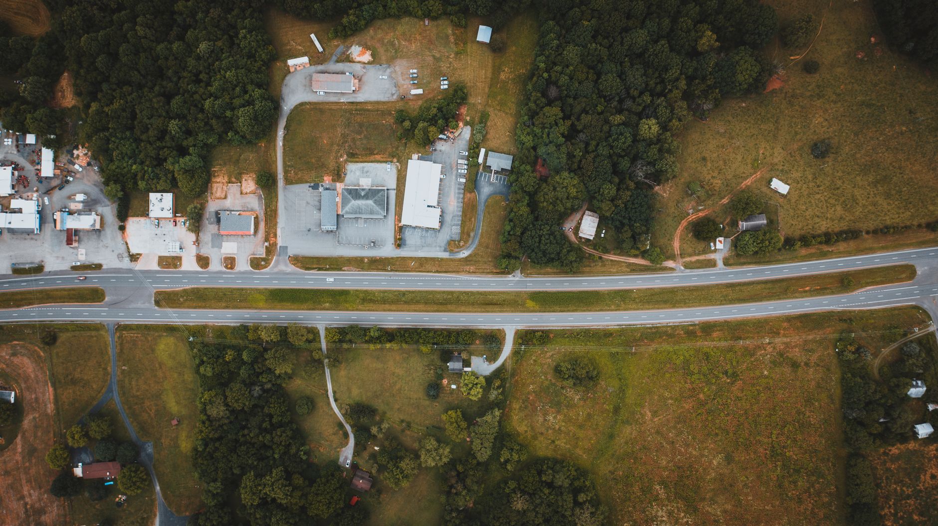 Overhead view of wavy roadways between green meadows with building roofs and trees in suburb