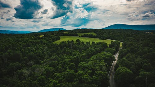 Aerial view of roadway between greenery woods and lawn behind ridge in overcast weather