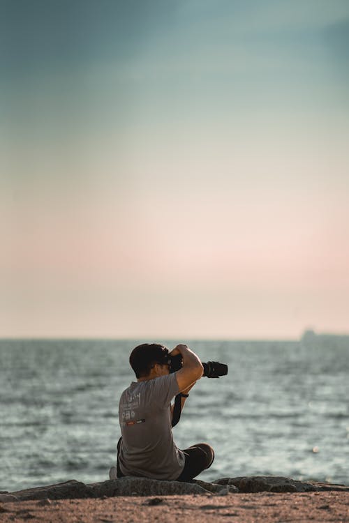 Person Sitting On Seashore Taking Picture