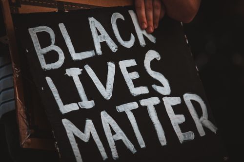Free Crop unrecognizable social justice warrior behind placard with Black Lives Matter inscription in darkness Stock Photo