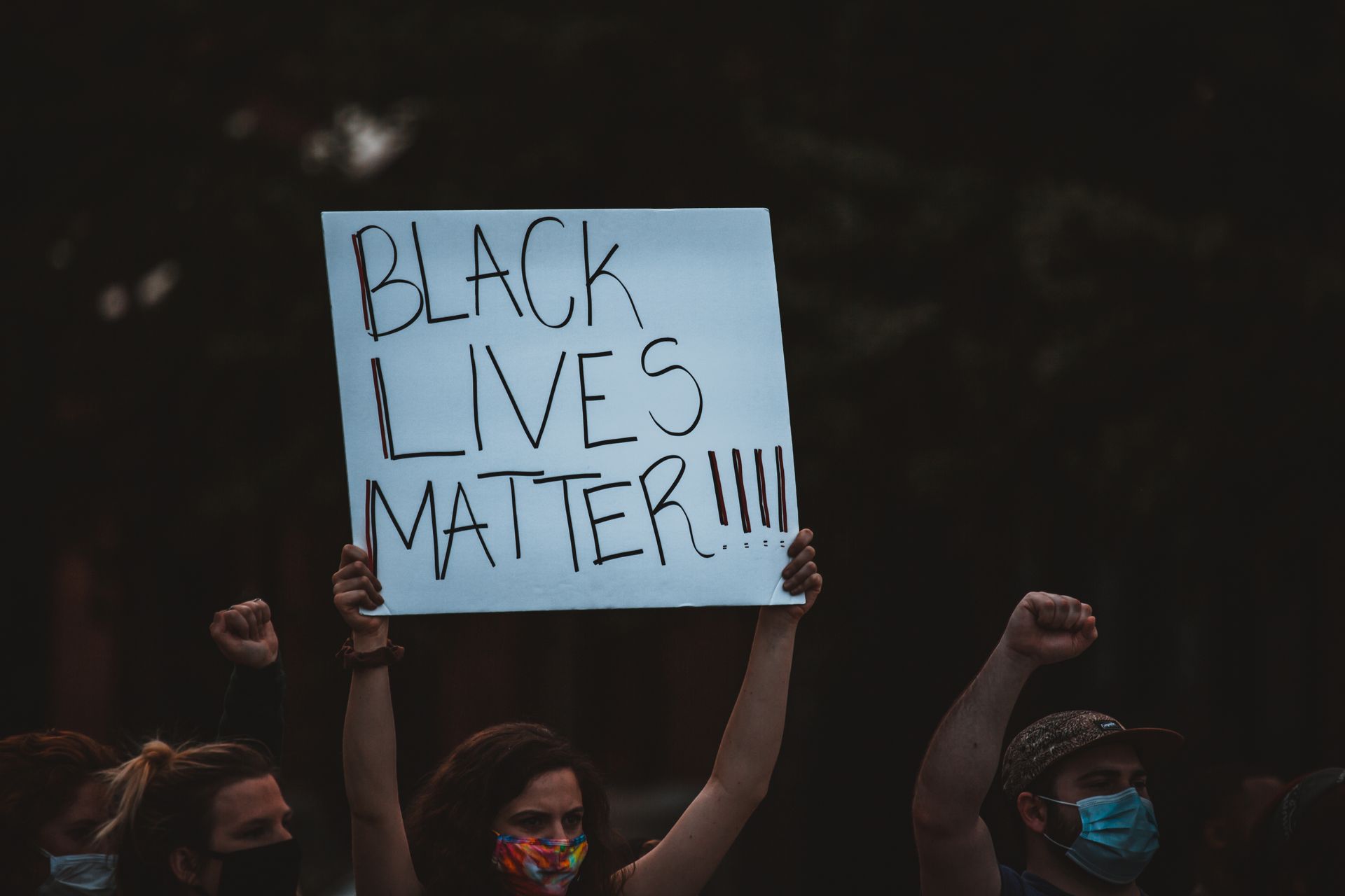 Anonymous social justice warriors in masks showing placard with Black Lives Matter title during manifestation in evening