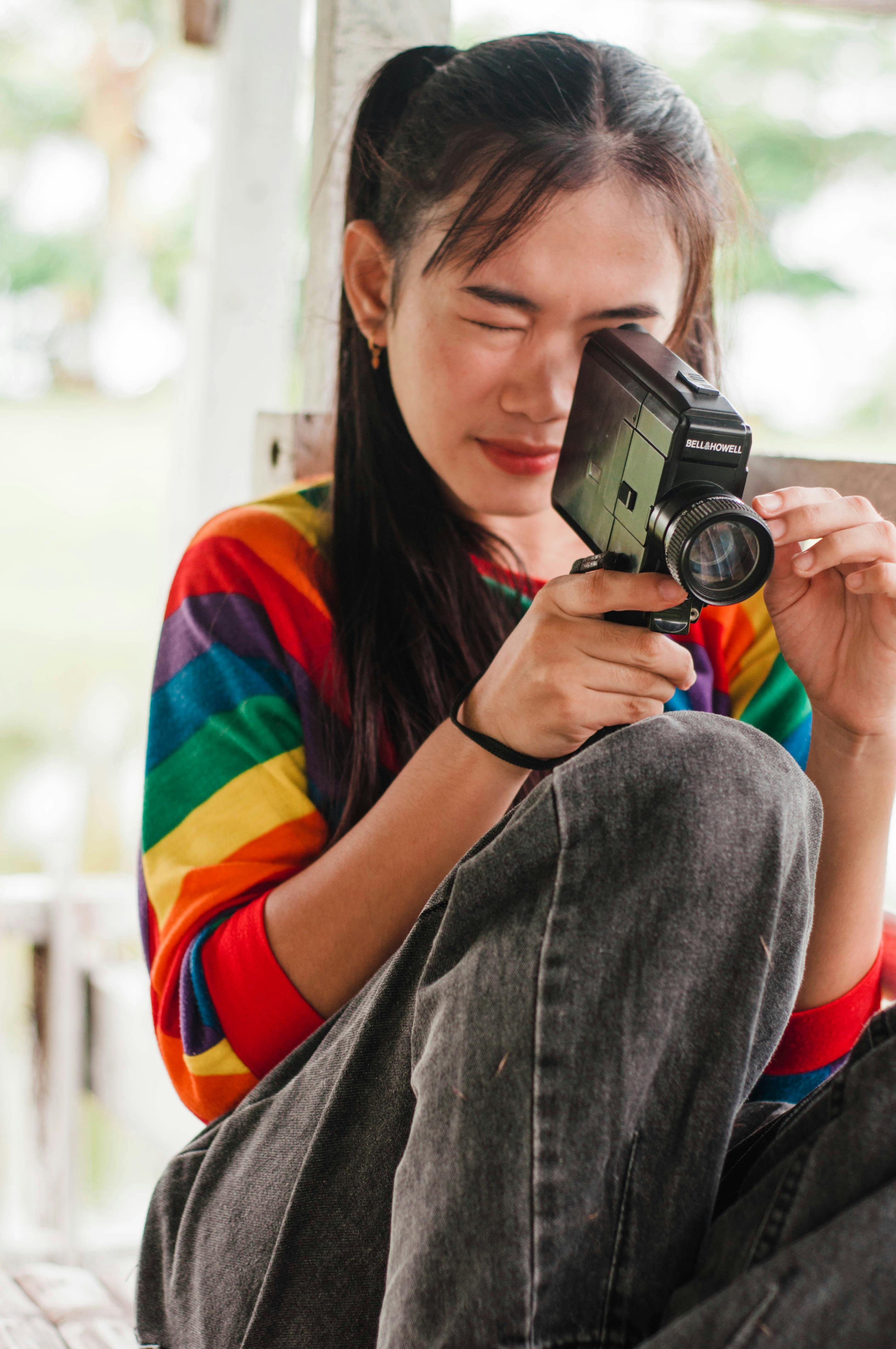 woman in gray denim pants and rainbow colored shirt using a vintage camera