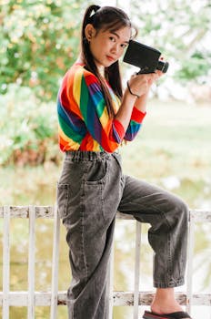 一位穿着彩虹毛衣的亚洲女子在户外拿着老式相机摆姿势