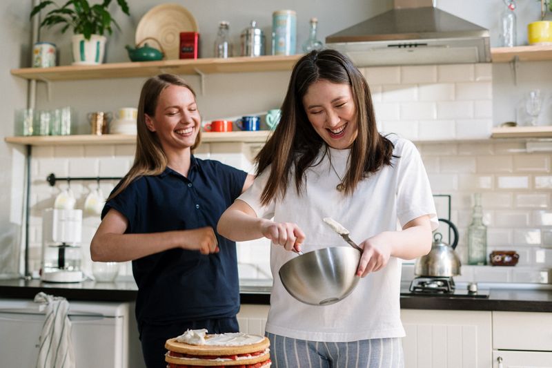 Two cooks laughing over a mixing bowl — photo by cottonbro studio on Pexels