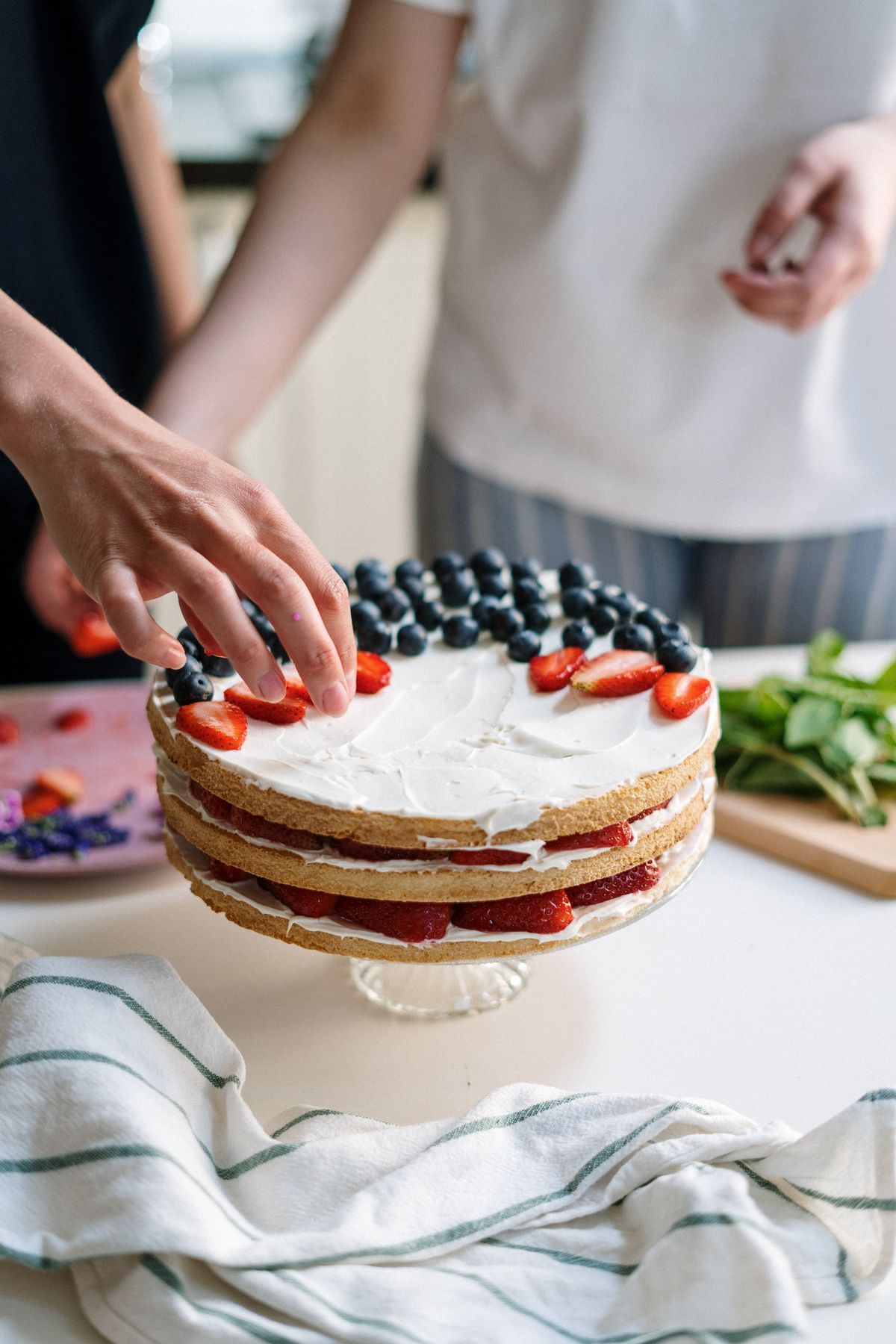 Close-up of a fresh berry cake being decorated with love and precision in a kitchen setting.