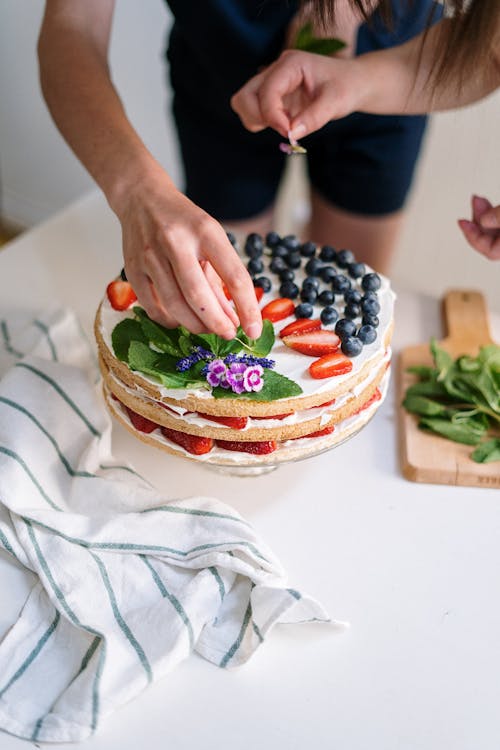 Person Decorating Cake with Different Berries 