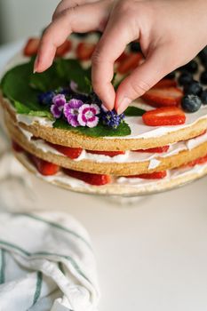 A beautifully decorated naked cake with strawberries, blueberries, and edible flowers being styled.