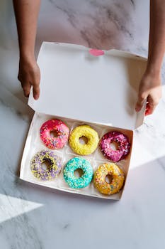 A top view of colorful, glazed doughnuts with sprinkles in a box, ready to enjoy.
