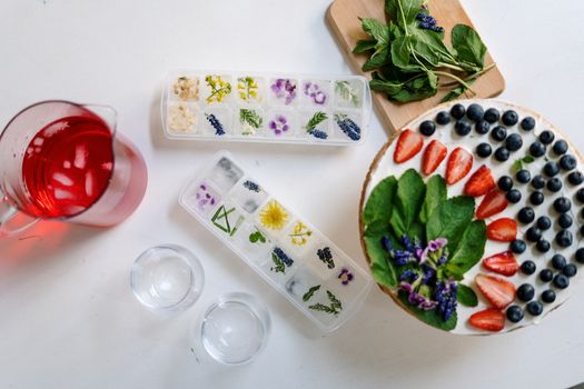 A colorful summer dessert with floral ice cubes, fresh berries, and mint on a flatlay.