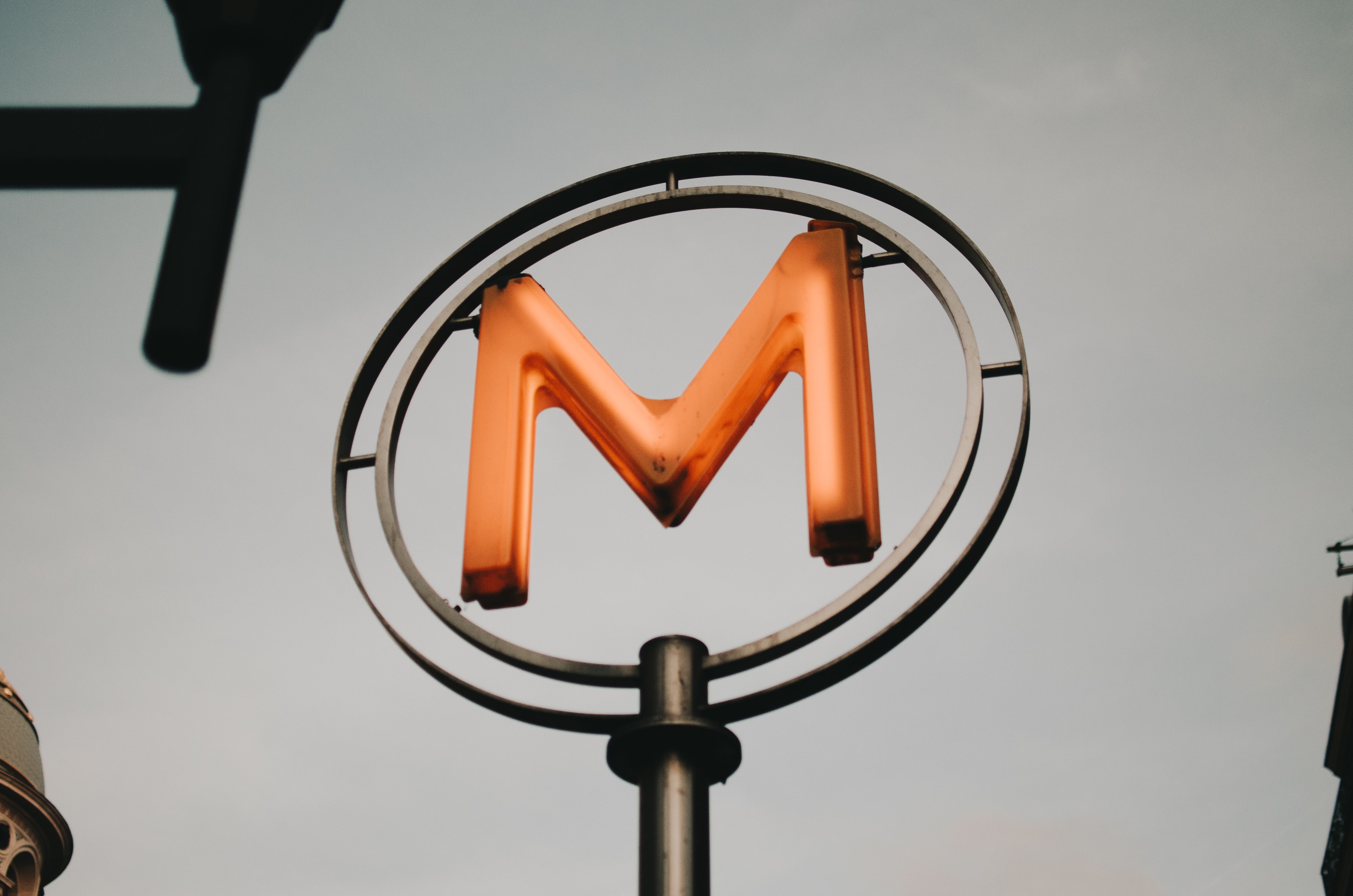 Low angle of modern neon signboard of metro on black metal pillar on city street against sky