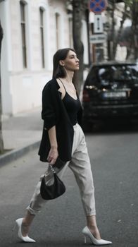 Full body of young female with dark hair in stylish clothes walking on street at daytime