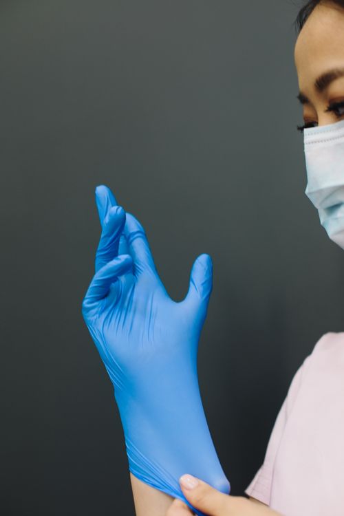 Free Close-up of a healthcare worker wearing gloves and a mask against a dark background. Stock Photo