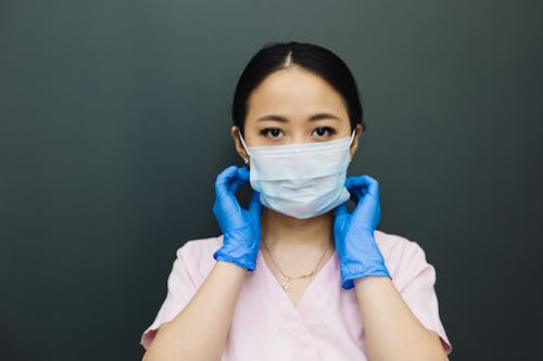 Woman in Pink Scrub Top With White Face Mask and Blue Latex Gloves