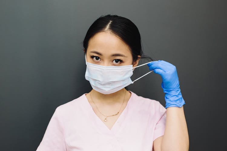 Woman In Pink Scrub Top Putting On A Face Mask