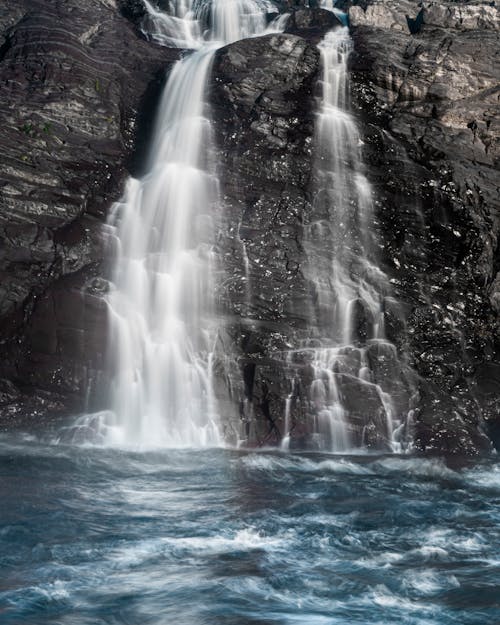 Cold fresh water falling from black stone cliff located near lake in nature