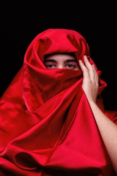 An artistic portrait featuring a person partially veiled by vibrant red satin, creating a mysterious allure.