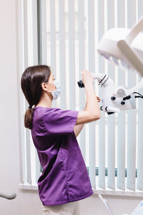 Free Woman in Purple Scrubs Fixing the Lens of a Dental Equipment Stock Photo