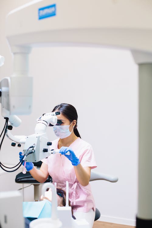 A Woman in Pink Scrub Suit Using Dental Equipment