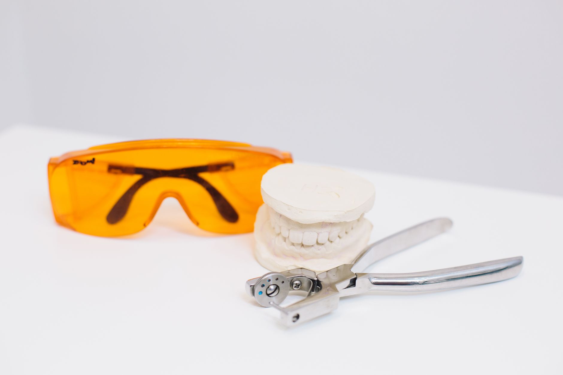 Close-up shot of dental tools, goggles, and tooth model on a white background.