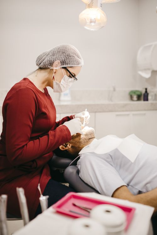 Free Side view of anonymous female stomatologist in eyeglasses and gloves checking teeth of lying man in clinic Stock Photo