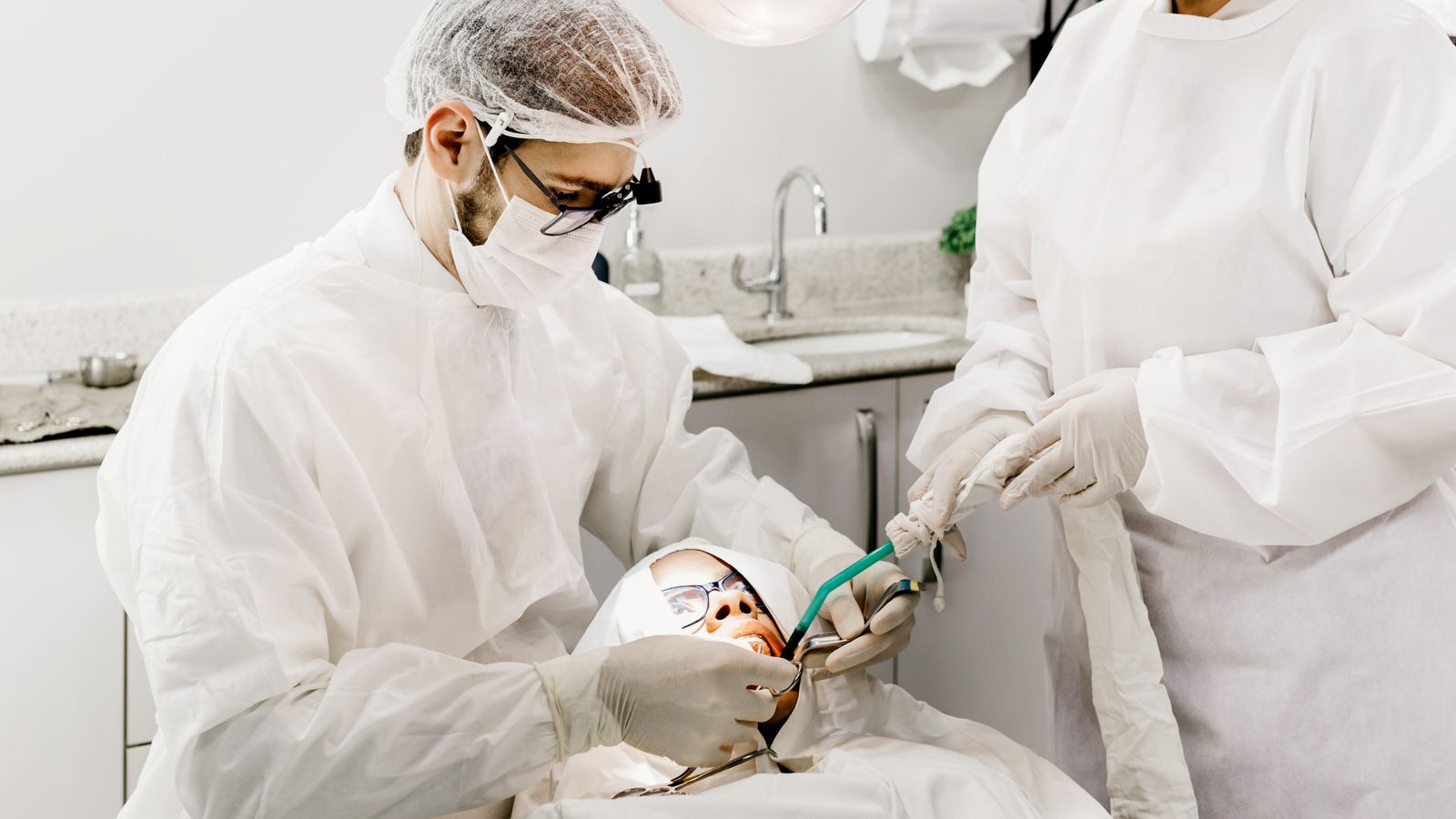 From above of unrecognizable male stomatologist and female assistant in uniforms treating patient teeth in clinic
