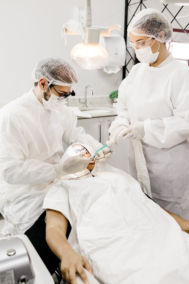 Unrecognizable Dentist With Assistant Treating Patient Teeth In Hospital