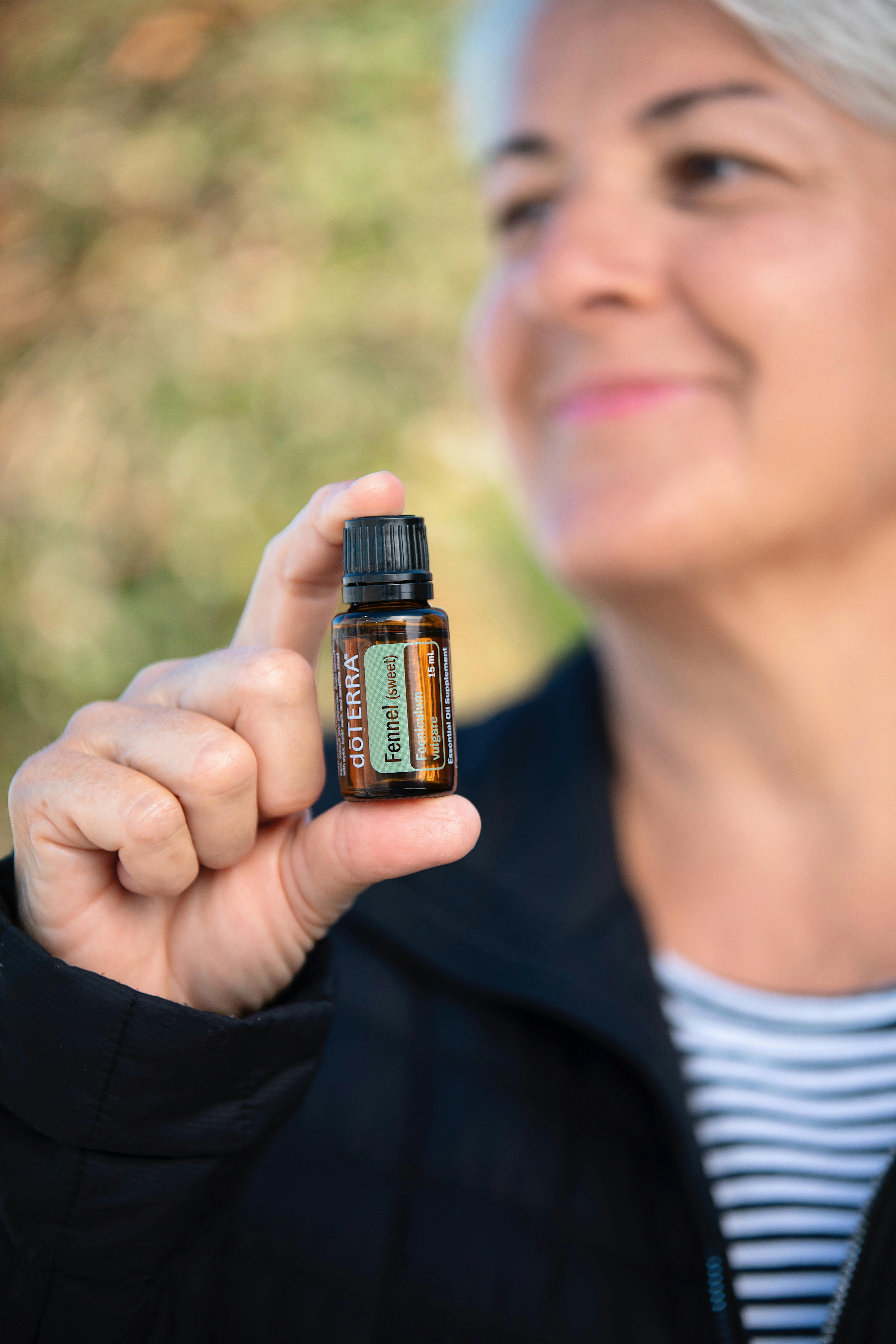 Senior woman smiling and holding a doTERRA fennel essential oil bottle, showcasing natural healing.