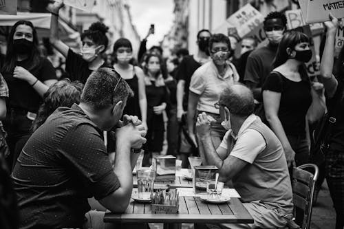 Grayscale Photo of a Small Group of People Sitting at a Table Looking at the Protesters
