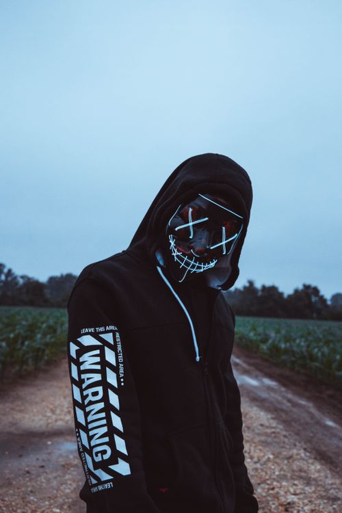 Free Eerie figure in a hoodie and mask on a rural path under cloudy skies. Stock Photo