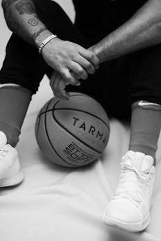 A black and white image of a seated basketball player holding a basketball.