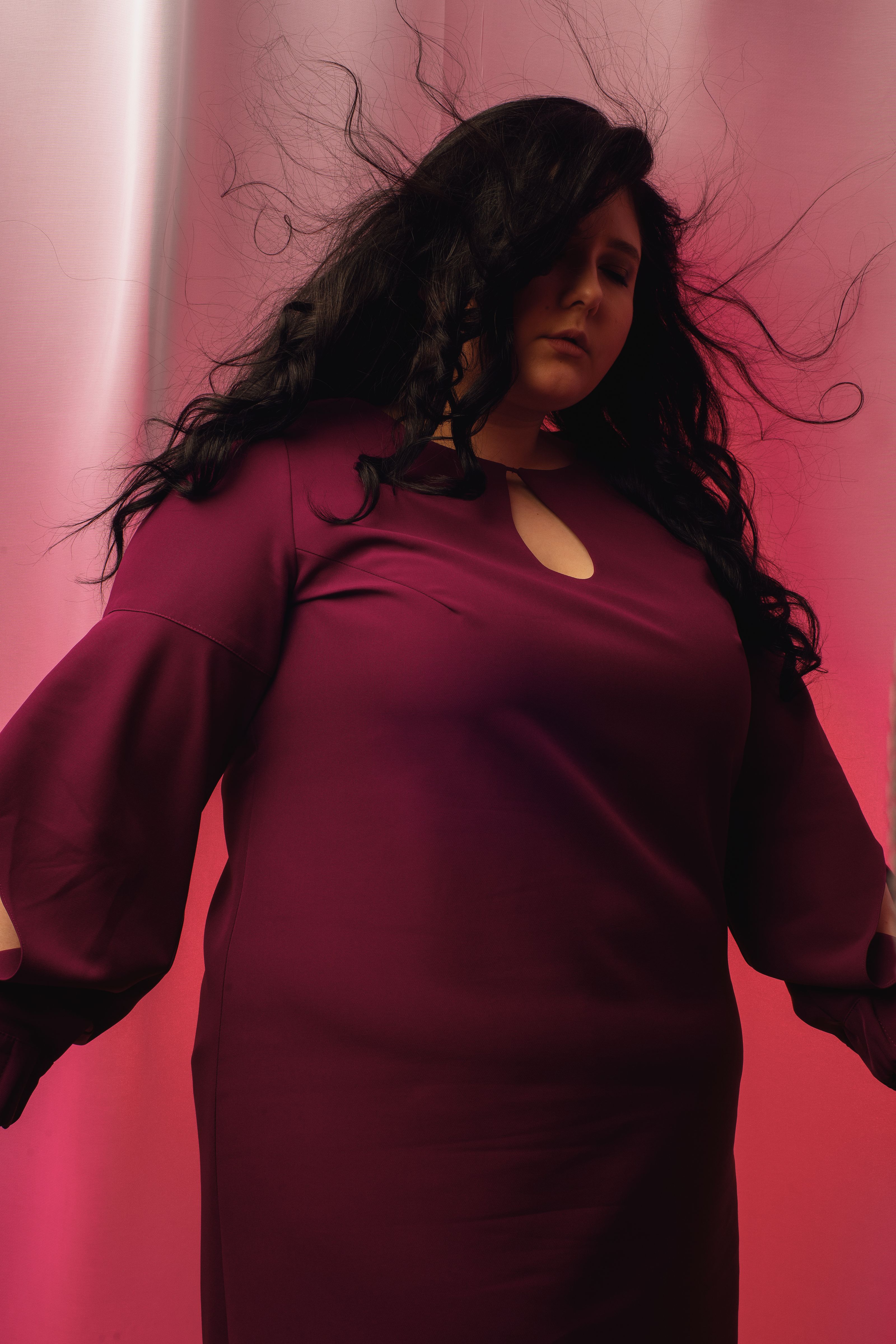 Retrato cativante de uma mulher em um vestido bordô posando contra um fundo gradiente.