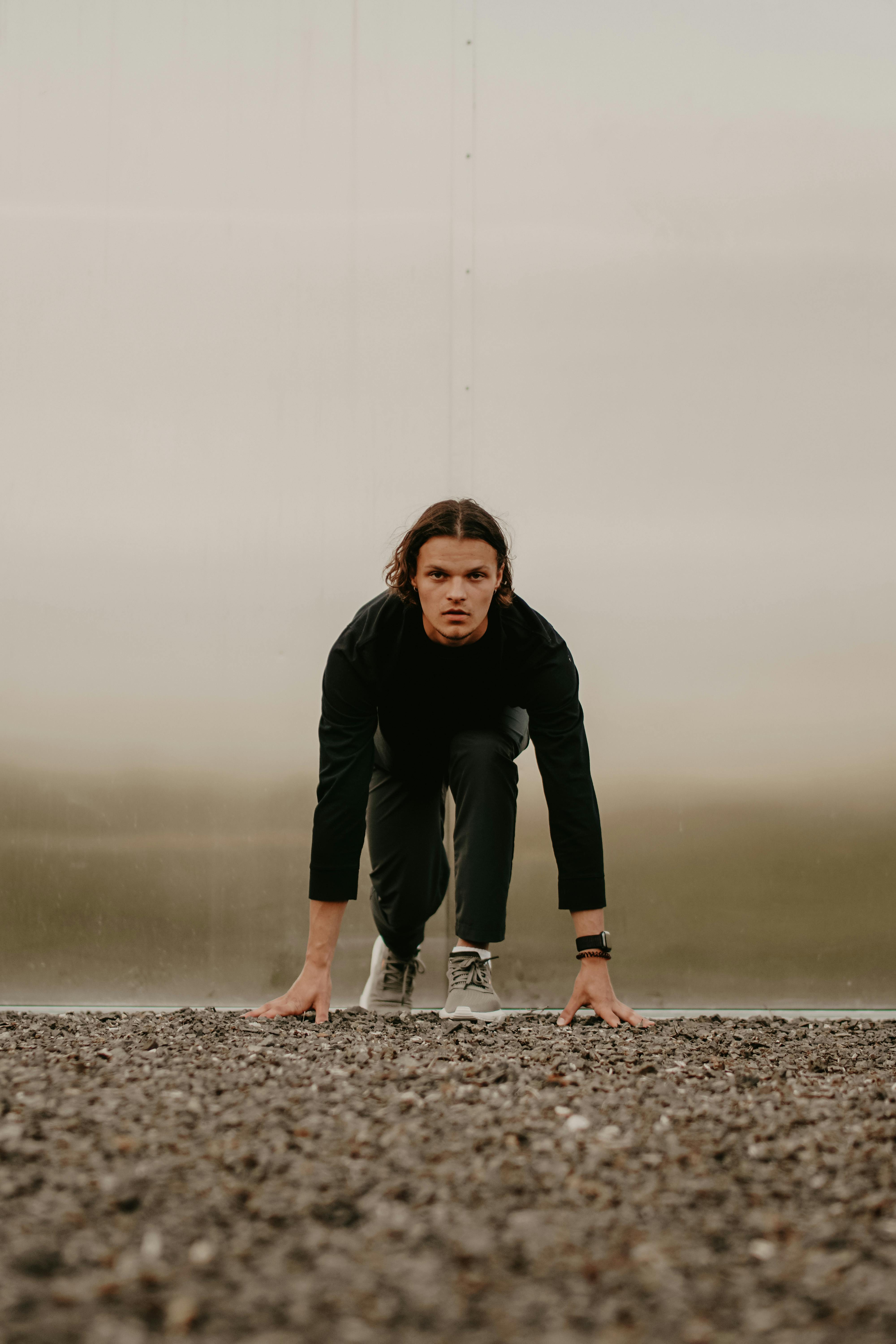 Adult male athlete in black attire preparing to sprint on a gravel track.