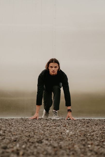 Adult male athlete in black attire preparing to sprint on a gravel track.