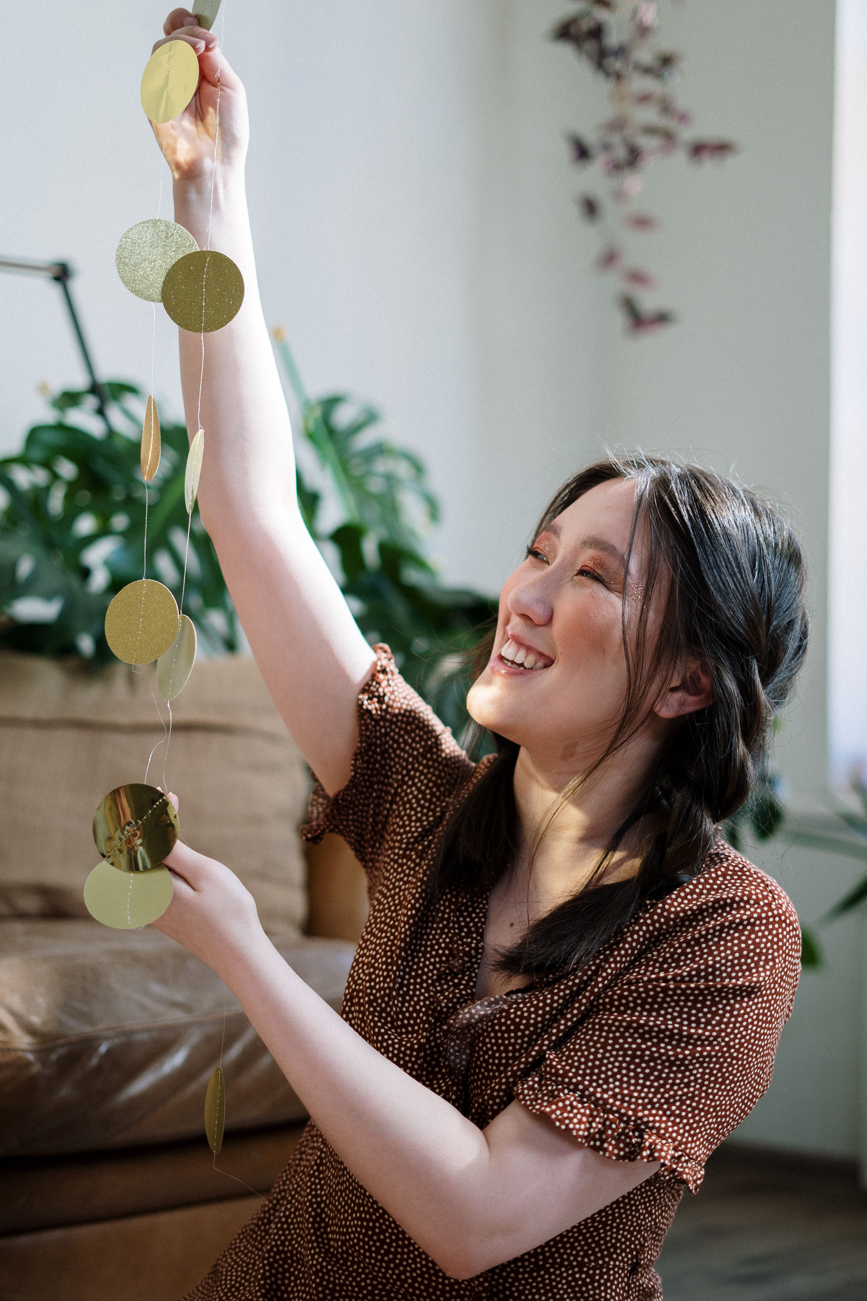 Young woman joyfully decorating indoors with a golden garland, sitting on a sofa.
