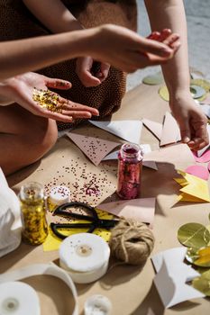 Close-up of hands crafting with colorful paper, glitter, and ribbons; perfect for DIY art projects.