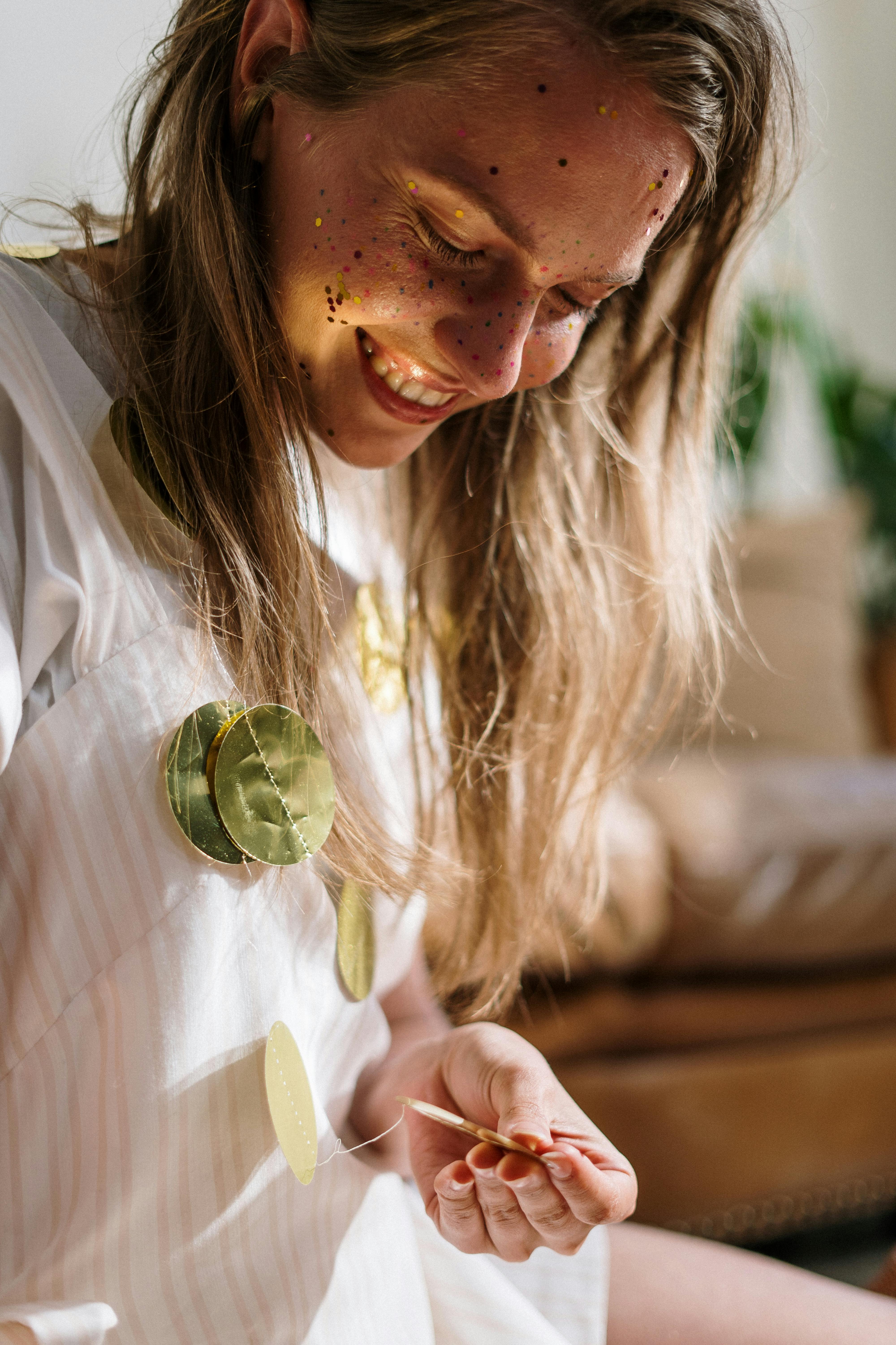 A young woman joyfully crafting a glittery garland in a cozy indoor setting.