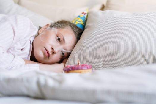 A person in pajamas lays in bed with a party hat and donut, reflecting on a quiet birthday.