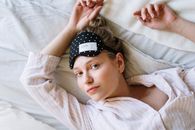 一名年轻女子穿着睡衣、戴着眼罩，在床上舒适地醒来，享受着一个轻松的早晨