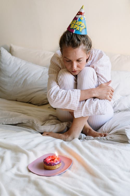 Woman in Pink and White Striped Long Sleeve Shirt Sitting on Bed