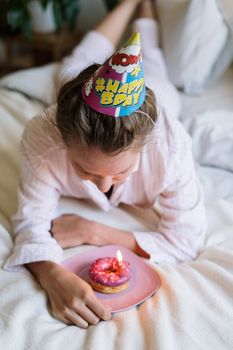 一位穿着睡衣的年轻女子在舒适的卧室里，用甜甜圈和蜡烛庆祝生日