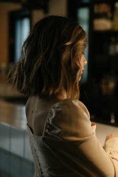 A thoughtful woman with short hair sits at a dimly lit bar counter.